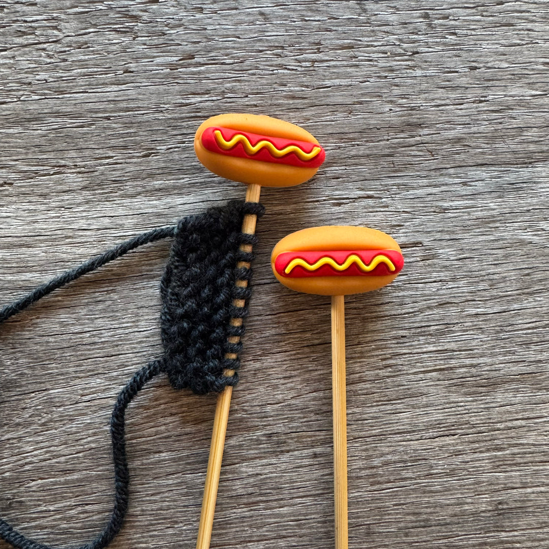 Hot dog-shaped stitch stoppers on wooden knitting needles.