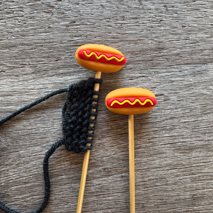 Hot dog-shaped stitch stoppers on wooden knitting needles.