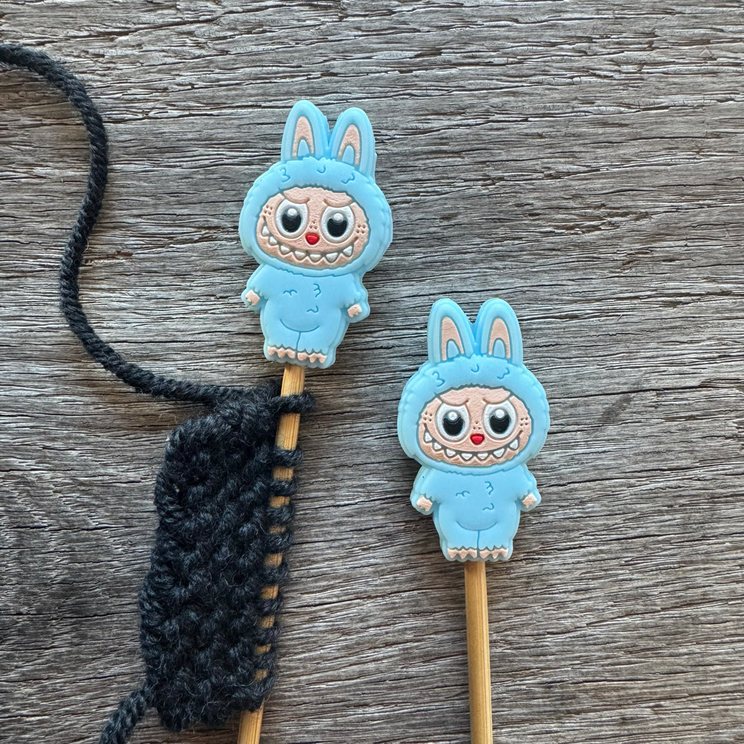 Two blue cartoon character monsters on sticks with a black string on a wooden surface.