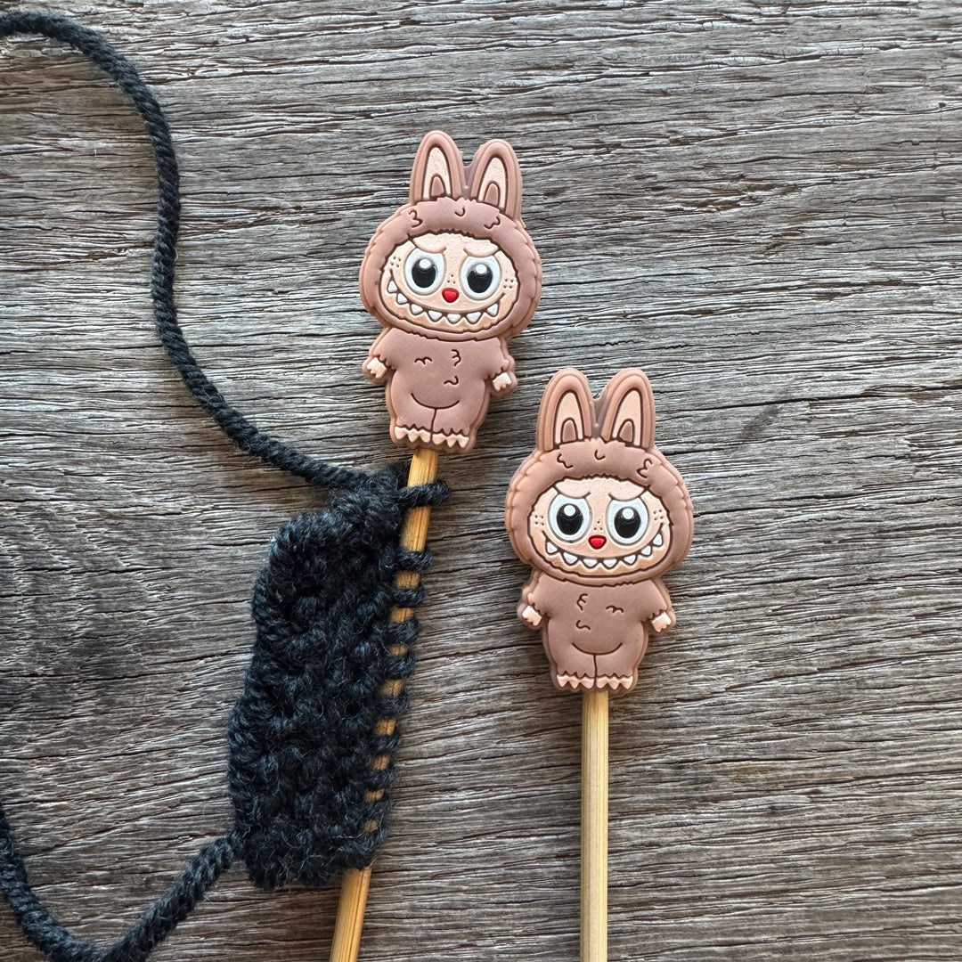 Two cartoon character monsters on sticks with a black string on a wooden surface.