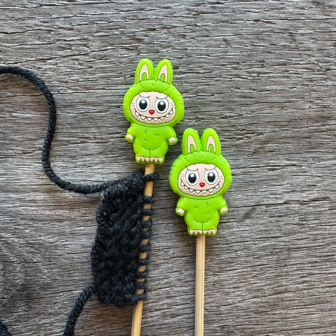 Two green cartoon character monsters on sticks with a black string on a wooden surface.