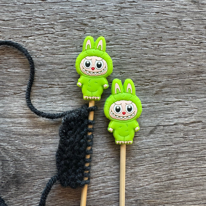 Two green cartoon character monsters on sticks with a black string on a wooden surface.