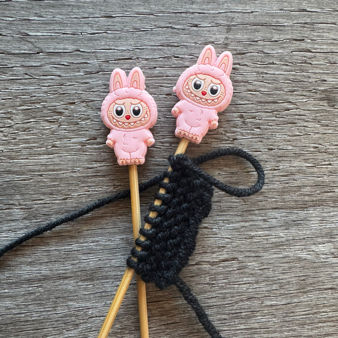 Two pink cartoon character monsters on sticks with a black string on a wooden surface.