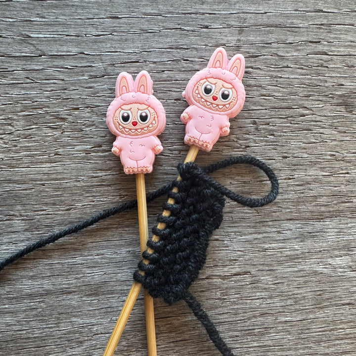 Two pink cartoon character monsters on sticks with a black string on a wooden surface.